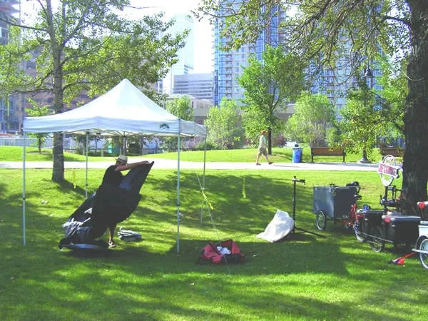 Joe's tent and mobile repair setup beside the Bow River Pathway with Calgary skyline
